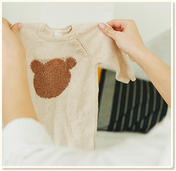 Someone holding a baby's romper with a bear silhouette embroidered.